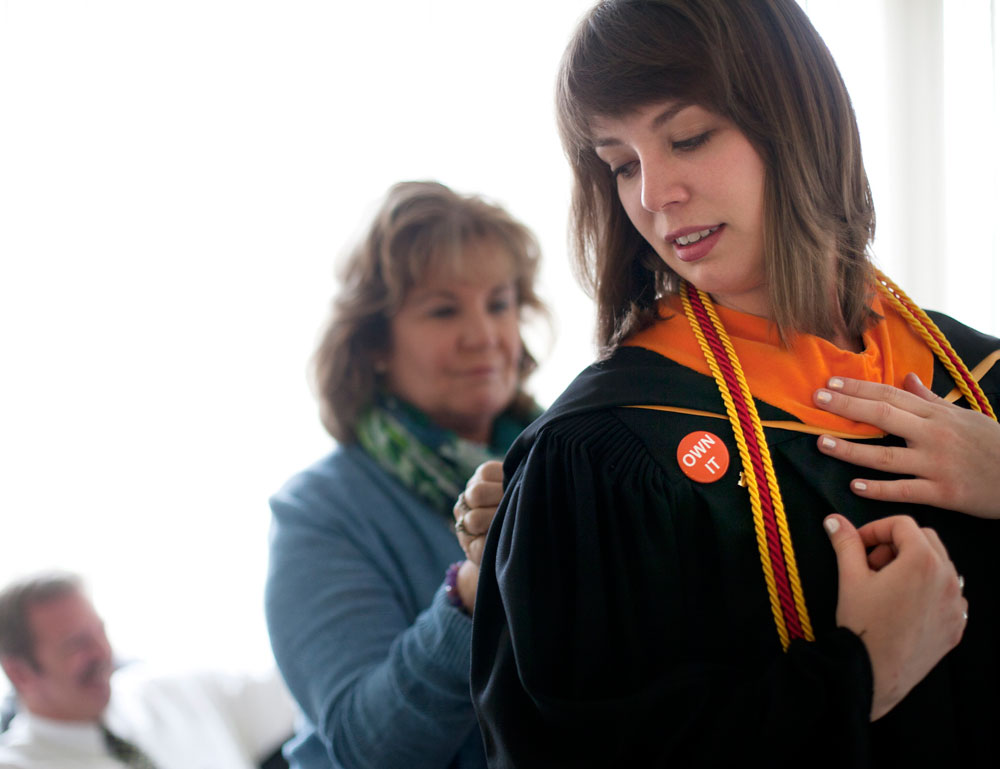 graduating student is assisted with her gown